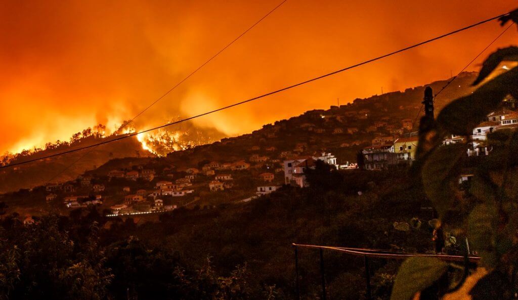 Visão noturna de uma colina pegando fogo ao lado de casas residenciais