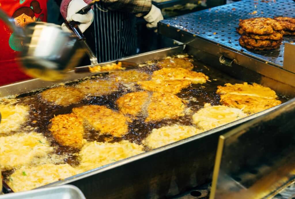 Imagem de uma tigela retangular cheia de óleo de comida, dentro da qual há vários bolinhos sendo fritos