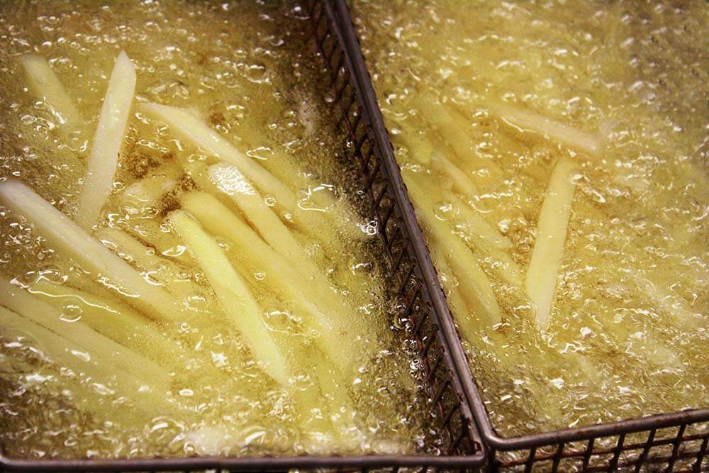 Foto de batatas em tiras sendo fritas em dois recipientes cheios de óleo de cozinha.