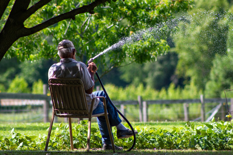 Foto de homem regando a grama com mangueira para ilustrar as cinco maneiras fáceis para não desperdiçar água em casa. Foto: Laney Smith/Unsplash