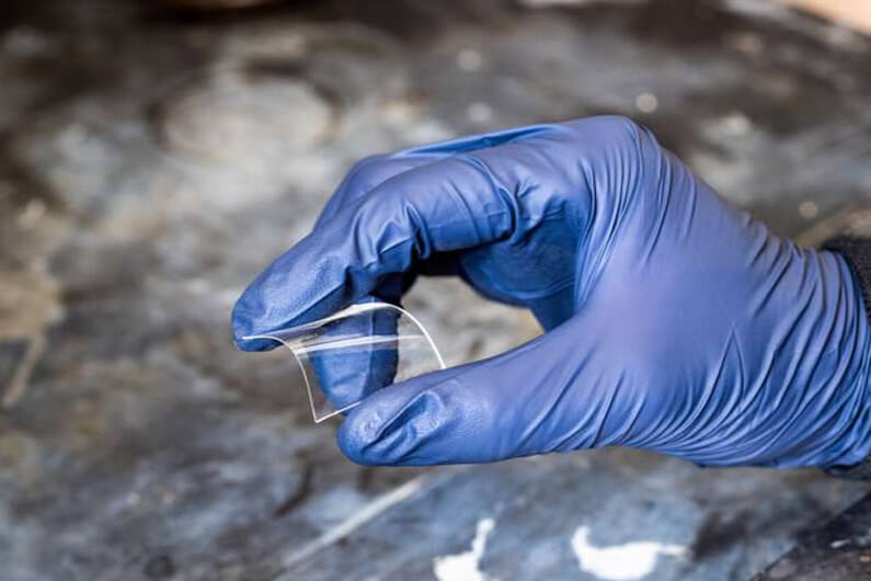 Imagem de uma mão vestida com uma luva, segurando um pequeno pedaço de plástico para ilustrar que reciclagem química fará plástico do futuro ter muitas vidas. Foto: Patrick Campbell/Universidade do Colorado, Boulder