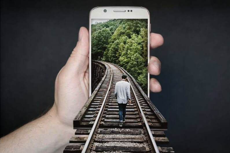 Imagem de um homem caminhando por um trilho com uma vegetação ao fundo sobre a tela de um celular para ilustrar artigo sore apas globais de plantas com acesso gratuito pelo celular. Foto: Pixabay.