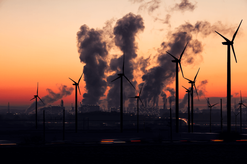 Imagem ao entardecer de uma fábrica soltando fumaça pelas chaminés ao fundo e turbinas eólicas como pano de frente para ilustrar que as turbinas eólicas também podem ser usadas para capturar CO2. Foto: Ralf Vetterle/GDJ/Pixabay