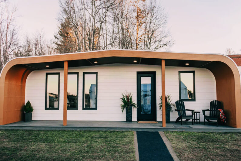 Imagem da fachada de uma casa, na cor branca com estruturas bege, para ilustrar artigo sobre uma casa impressa em 3D com produtos 100% florestais.