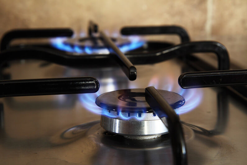 Foto parcial de um fogão a gás com duas bocas acesas para ilustrar post sobre sete dicas para proteger sua saúde ao cozinhar com gás.
