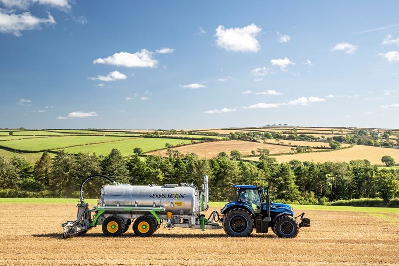 Foto ilustrativa de um novo trator movido a combustível oriundo de esterco bovino espalhando suplementos agrícolas na terra.