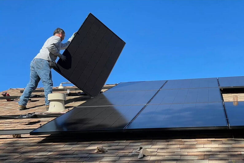 Foto de um homem, sobre o telhado de uma casa, instalando painéis solares como ilustração do artigo que aborda o futuro do trabalho na economia verde.