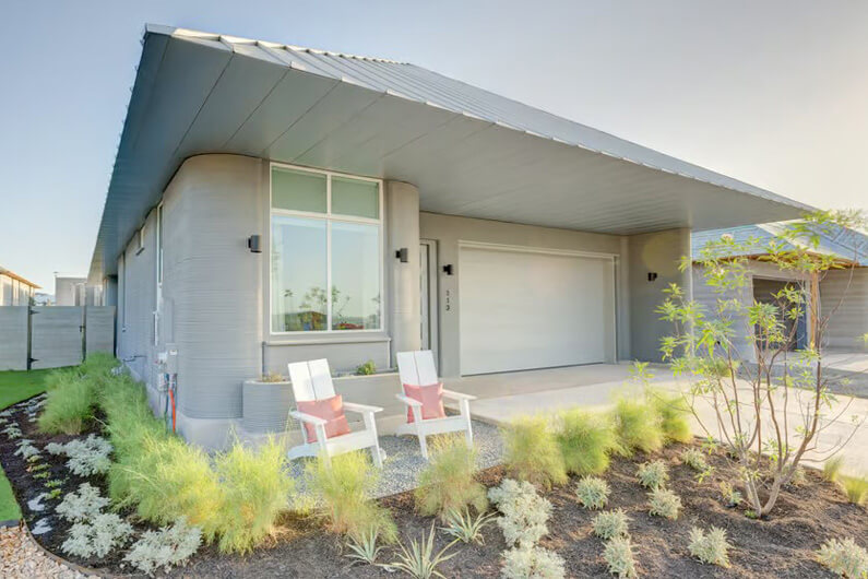 Imagem da fachada de uma casa, cinza claro, com um jardim na frente, serve de ilustração o post sobre o maior empreendimento residencial do mundo, impresso em 3D.