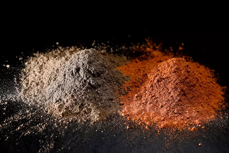 Imagem de dois montinhos de pó nas cores cinza e laranja para ilustrar o artigo cujo título diz que Um novo material pode mudar a forma como fazemos cimento.