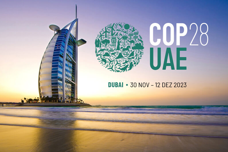Imagem de uma praia em Dubai mostrando o hotel Burj Al Arab com o logo da COP28 contrastando com o pôr do sol ilustram o post cujo título diz: O que é COP? Aqui está uma explicação prática.