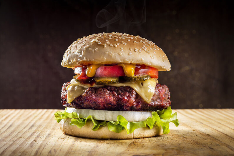 Foto de um sanduíche estilo cheeseburger com uma carne bem grossa, acompanhada de alface, tomate, queijo, picles e molho, para ilustrar título do artigo que diz que o consumo de carne pode diminuir se adotarmos rótulos ecológicos.