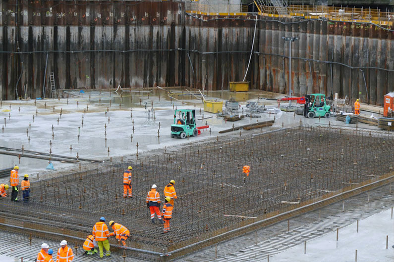 Foto de uma construção mostrando operários e uma ampla área concretada para ilustrar o post cujo título diz que substituir a areia pelo grafeno torna o concreto mais ecológico.