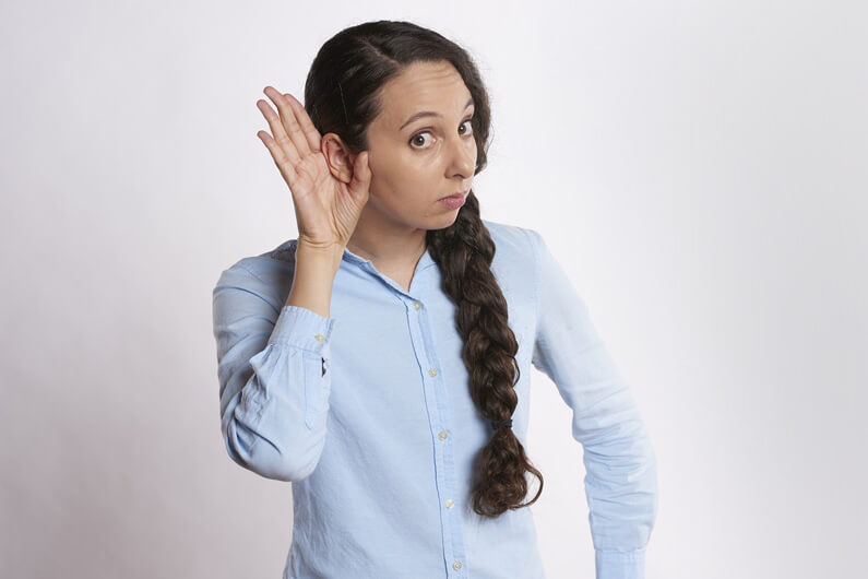 Imagem de uma mulher de cabelos escuros e com uma mão em forma de concha em volta de uma das orelhas ilustra post cujo título diz que a perda auditiva da idade e estilo de vida está perto de ser evitada.
