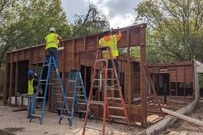 Imagem de trabalhadores ao ar livre desmontando uma construção de madeira para ilustrar post cujo título diz que cidades adotam a desconstrução para evitar lixo em aterros.