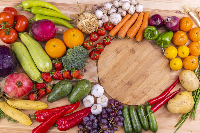Imagem bem colorida de vários legumes e frutas sobre uma mesa de madeira para ilustrar post cujo título diz que dietas veganas limpam o ar e podem salvar mais de 200 mil vidas.