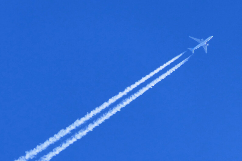 Imagem de um avião voando por um céu totalmente azul mostrando o rastro do combustível para ilustrar post cujo título diz que o Brasil se prepara para produzir combustível sustentável de aviação.