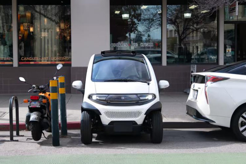 Imagem de um micro veículo elétrico estacionado numa vaga apertada numa rua do centro de uma cidade ilustra o post cujo título diz que um microcarro elétrico estreará nas ruas dos EUA ainda este ano.